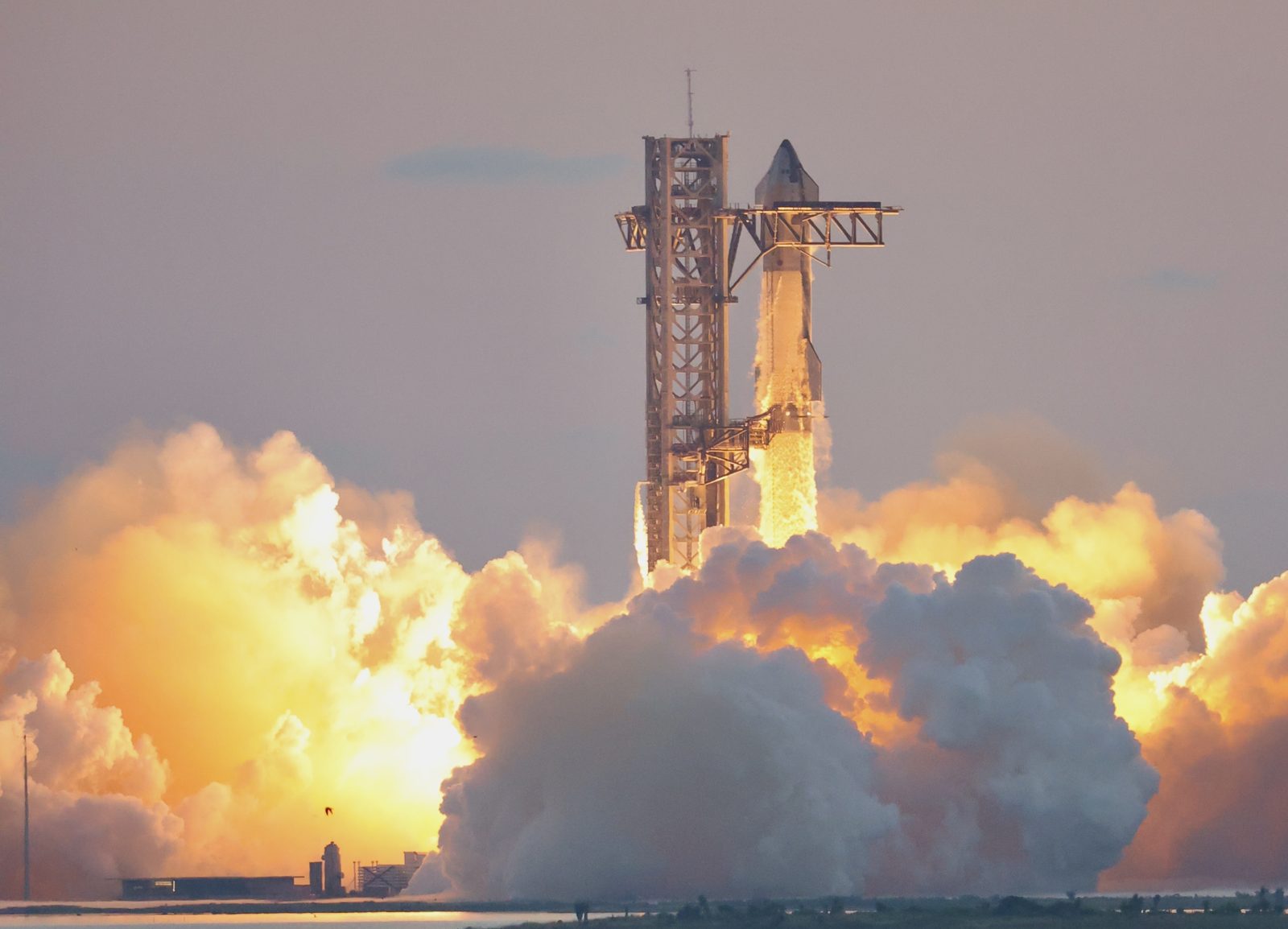 SpaceX's Starship lifting off beside its launch tower in low golden sun on its fifth flight test, in October 2024, with clouds of exhaust spreading across the pad