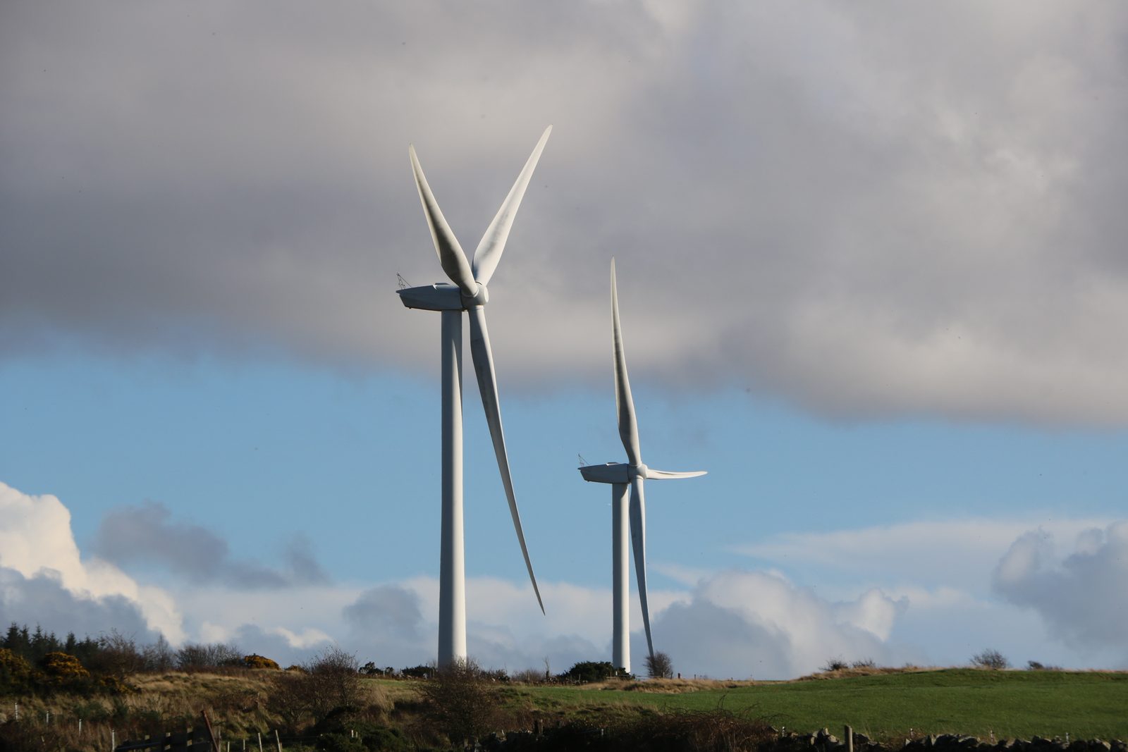 Two wind turbines on Barlockhart Moor, near Glenluce in Dumfries and Galloway, in November 2022, under heavy grey cloud with a strip of blue sky below it